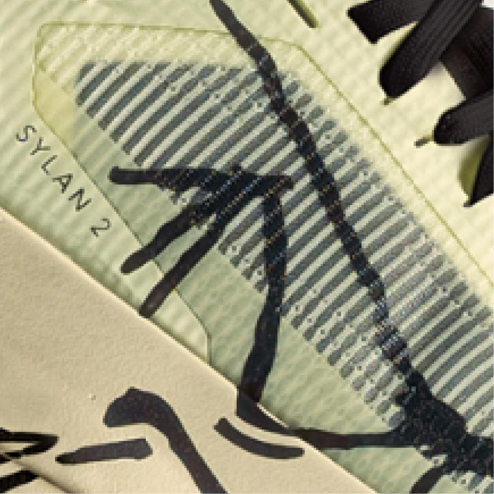 Close-up of a light green shoe detail showing "SYLAN 2" text, black laces, a striped translucent overlay, and irregular black markings.