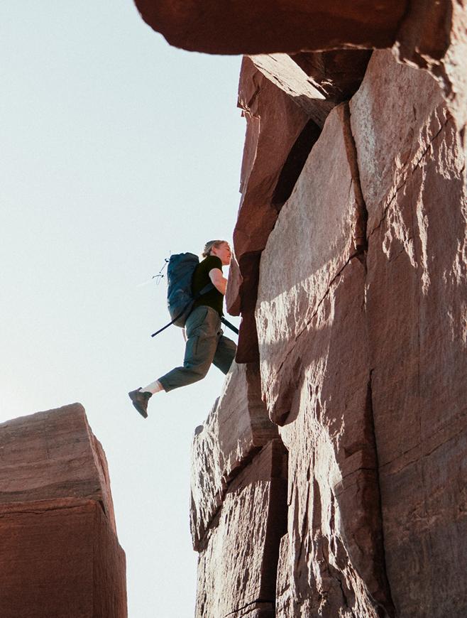 Person with backpack leaping between two rock formations.