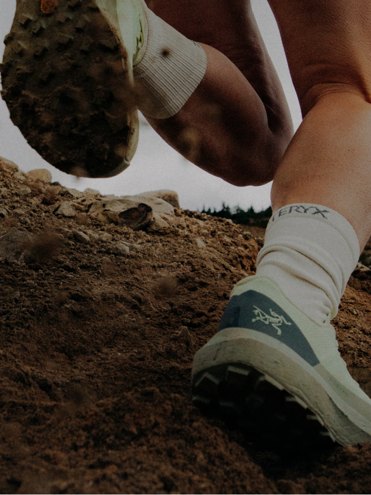 Trail runner's legs in Arc'teryx socks and shoes climbing a rocky dirt hill.