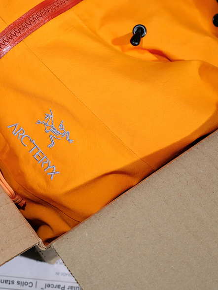 Orange Arc'teryx jacket with logo, partially in a cardboard box.