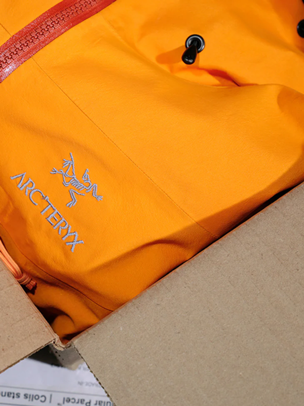 Orange Arc'teryx jacket with logo, partially in a cardboard box.