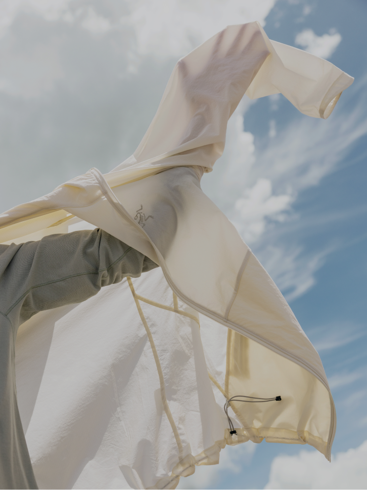 An off-white Arc'teryx jacket billows against a bright, cloudy sky.
