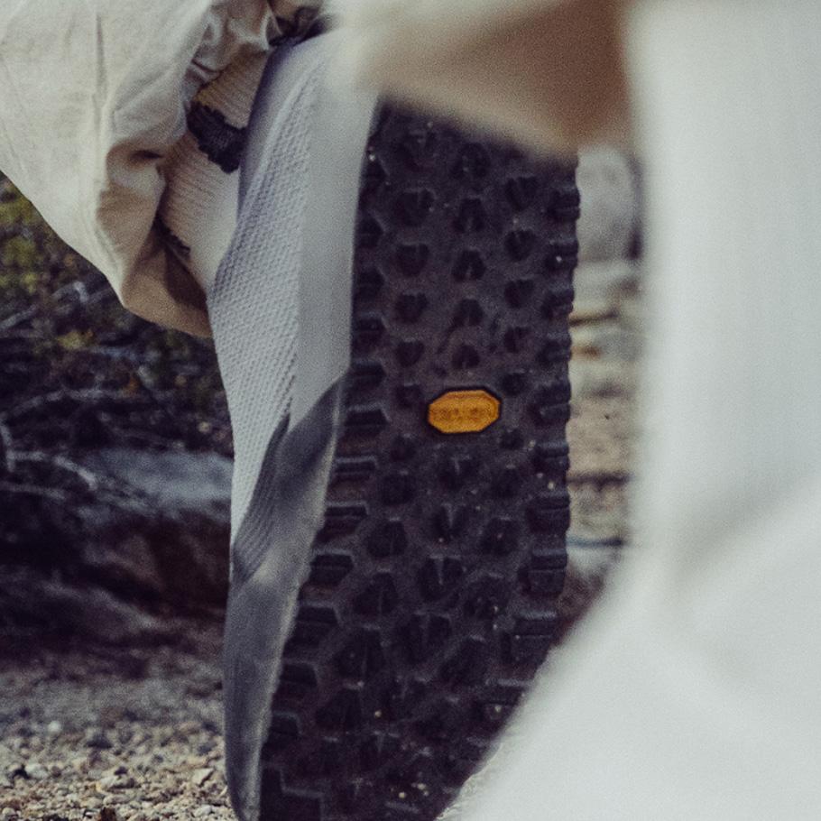 Close-up of a shoe's rugged black sole with a yellow Vibram logo on an outdoor trail.