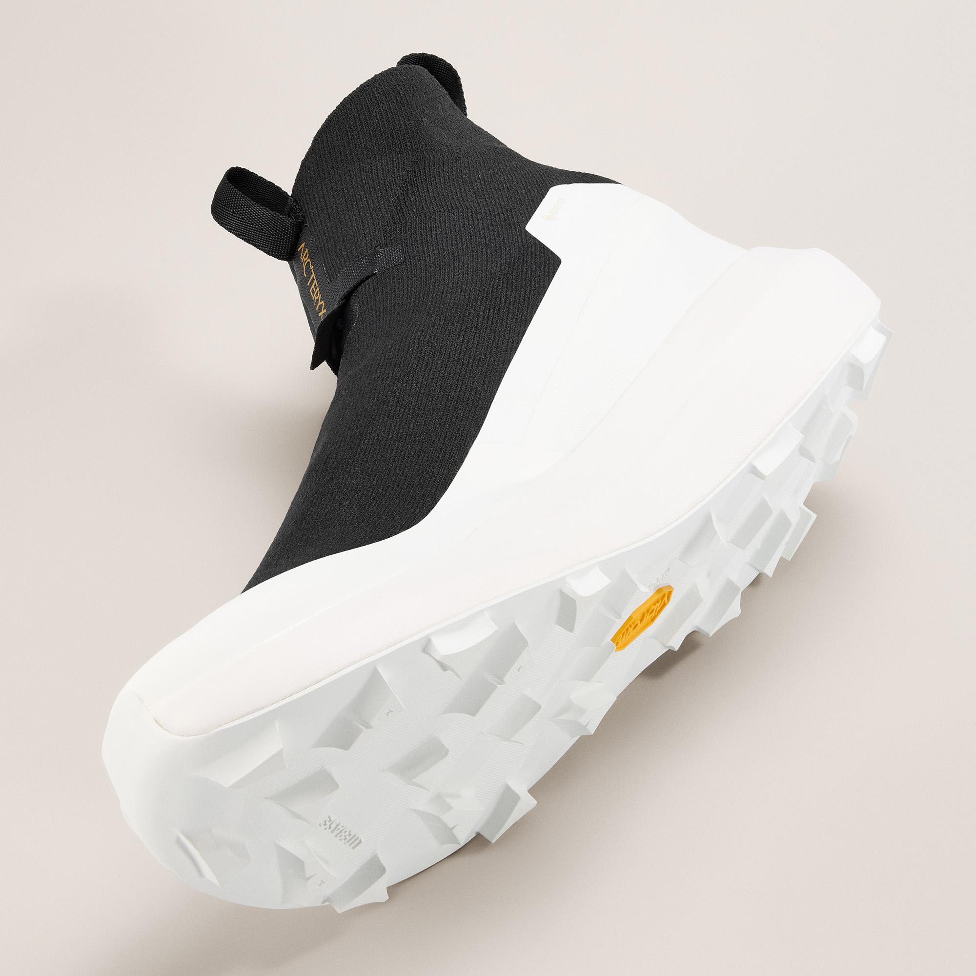 a pair of black and white sneakers with a white sole on a white surface .