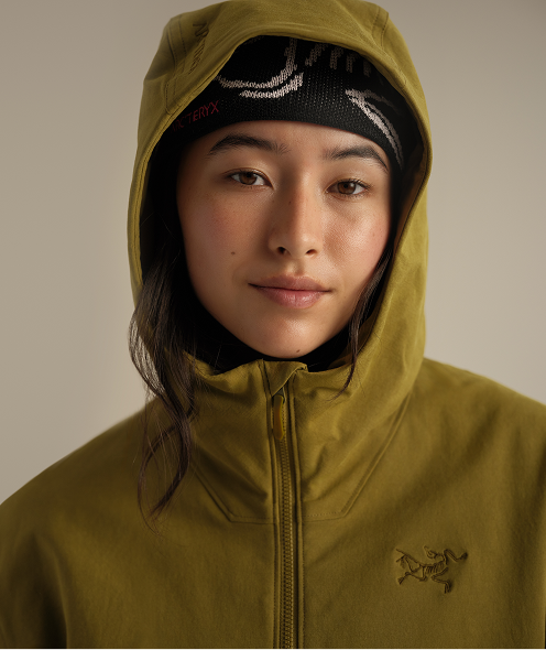 A woman in an olive green Arc'teryx hooded jacket and a black beanie looks forward.