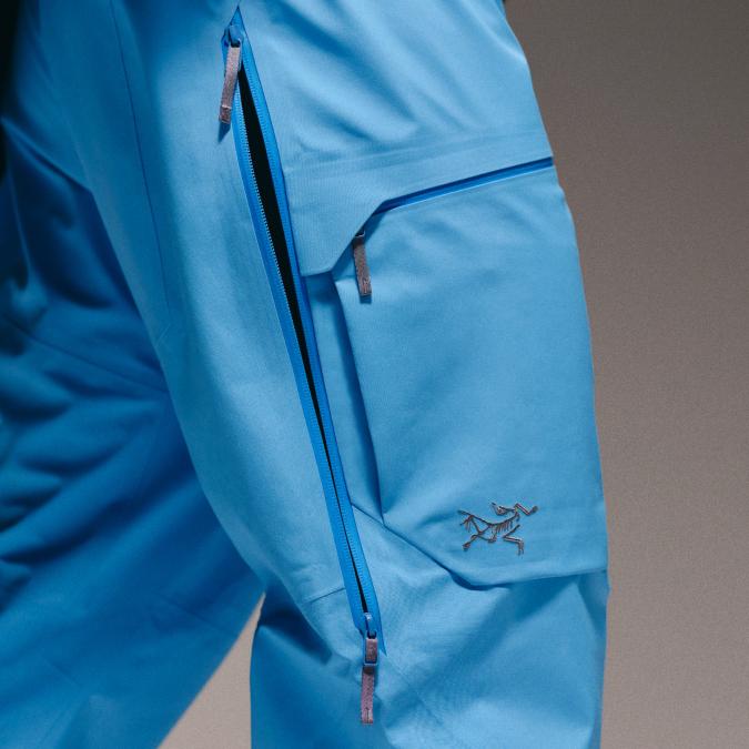 Close-up of bright blue Arc'teryx outdoor pants with a partially unzipped side vent and a thigh pocket.