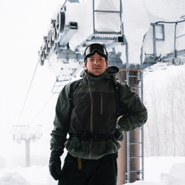 a man wearing a ski jacket and goggles stands in front of a ski lift