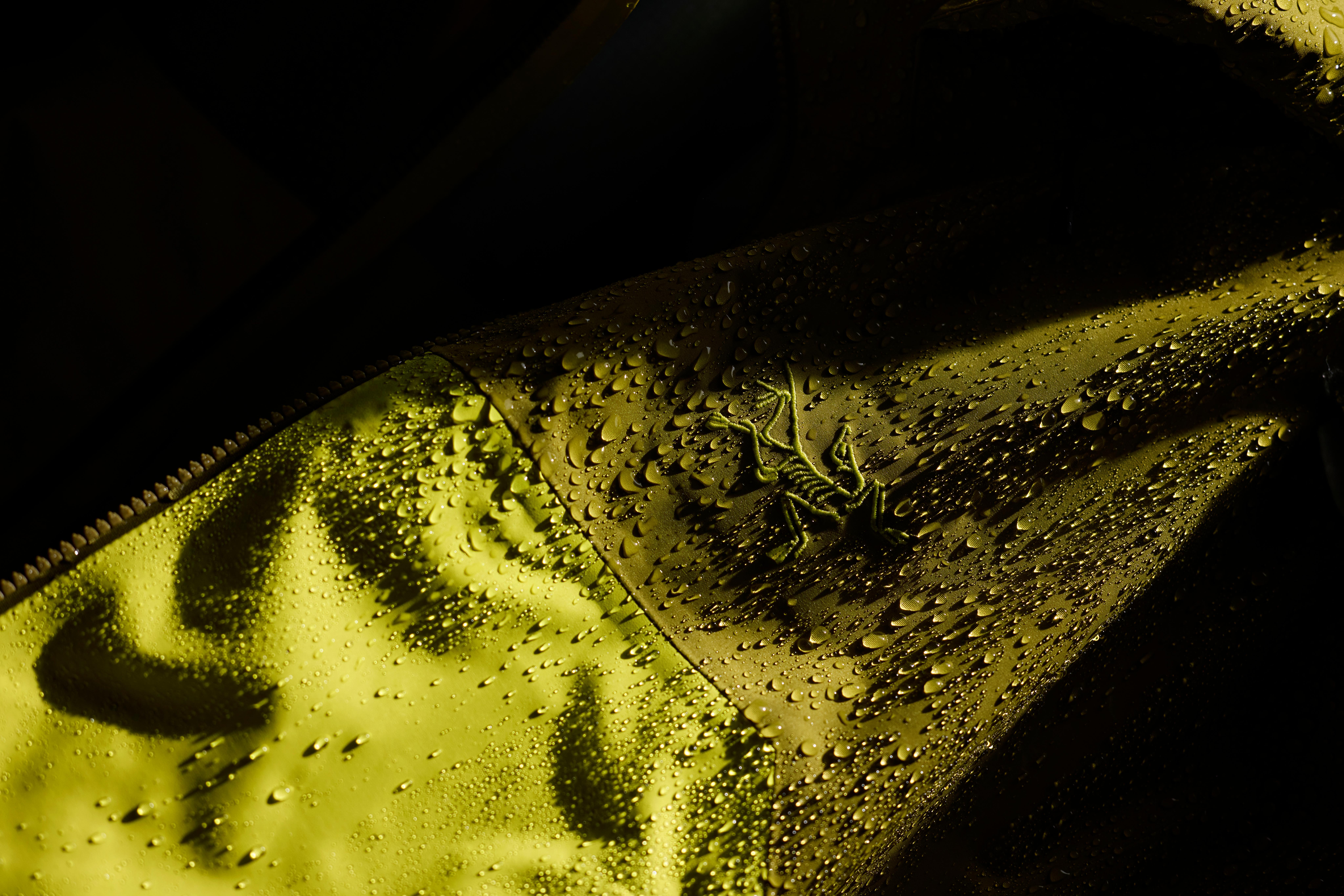 Water droplets bead on a yellow Arc'teryx jacket fabric.