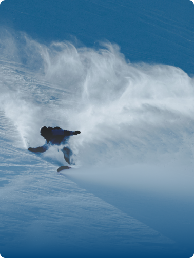 A snowboarder carves through snow, kicking up a large cloud of powder on a mountain slope.