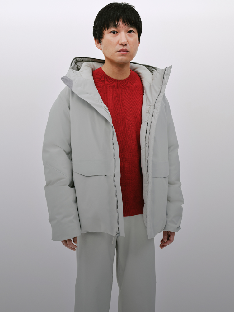 Man wearing a light gray puffer jacket over a red sweater and light gray pants.