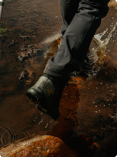 A person's boot splashing into muddy water.
