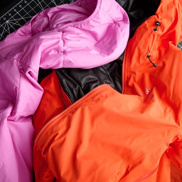 Pink, orange, and black jackets laid on a black grid mat.