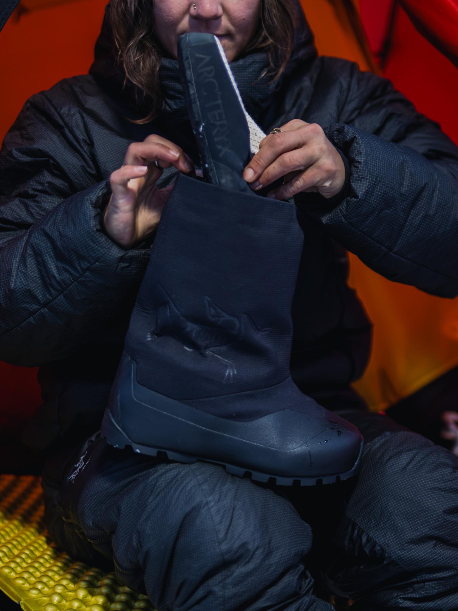 A person inserts an Arc'teryx liner into a dark insulated boot.