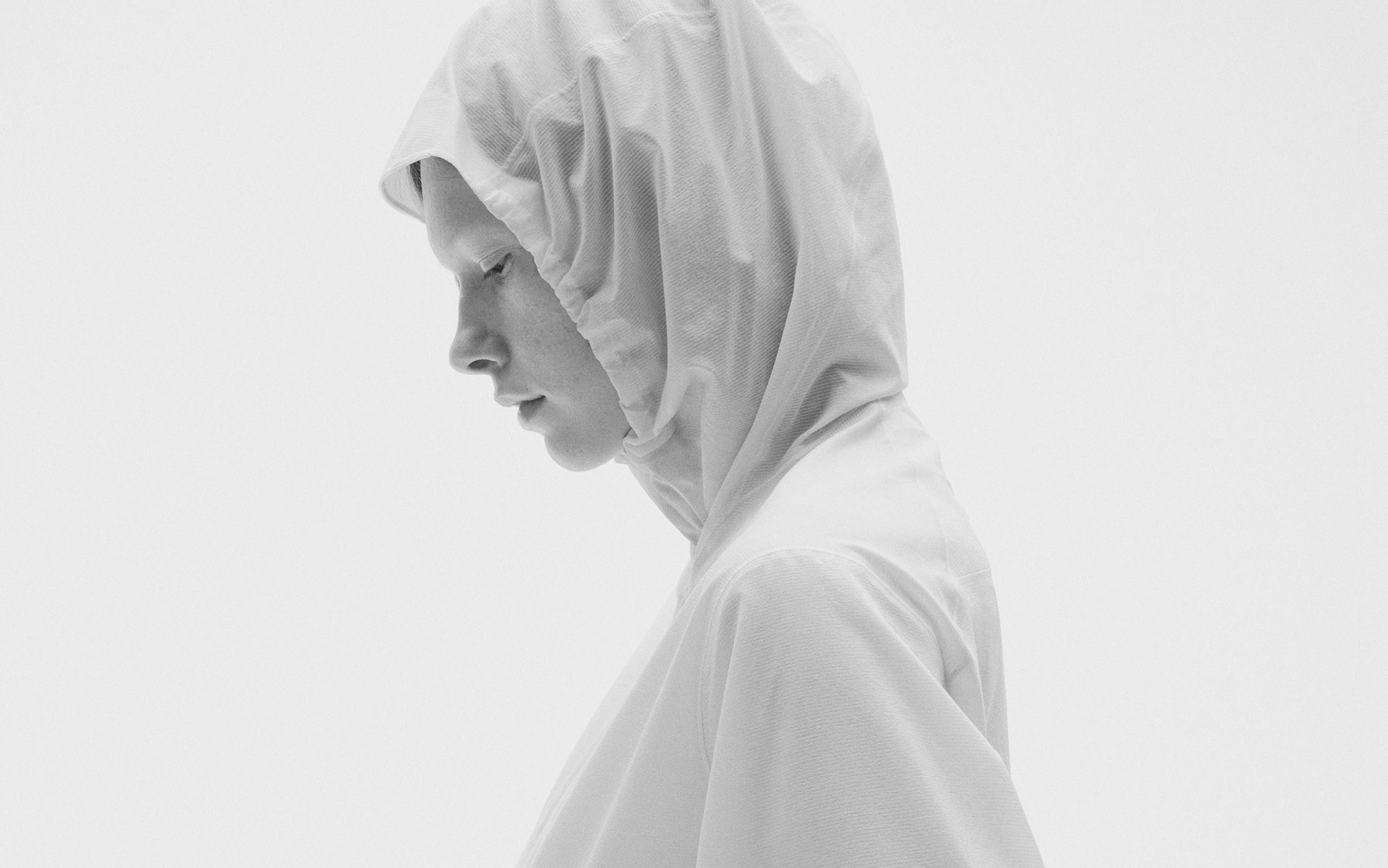 Monochrome profile of a person in a white hood looking down.