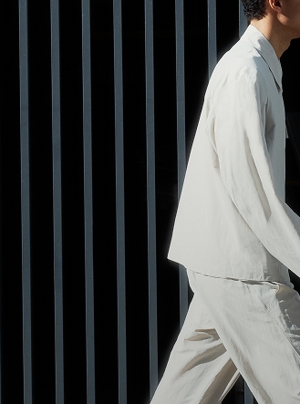 A person in a light outfit walks past a dark background with vertical bars.