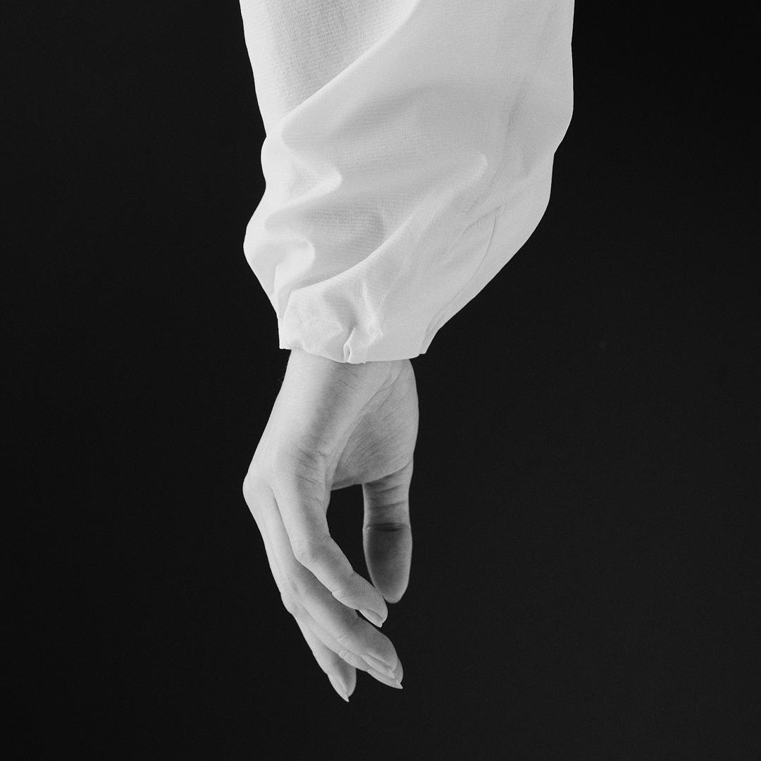 Monochrome image of a hand extending downwards from a white cuffed sleeve against a dark background.