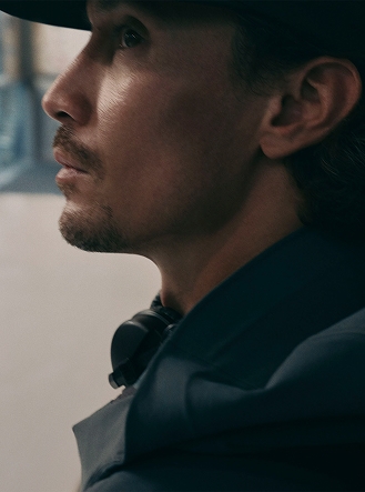 Close-up of a person in a light grey hooded jacket, looking up, with dramatic lighting on their face.