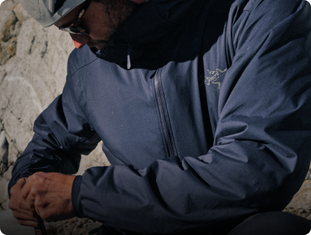 Close-up of a person in a dark blue Arc'teryx jacket and helmet, tying gear.