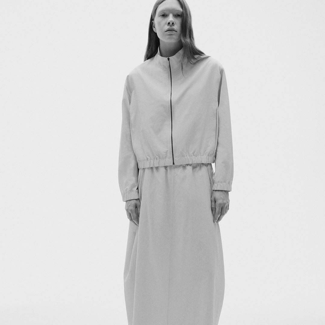Monochrome shot of a model wearing a light cropped zip-up jacket and a long skirt.