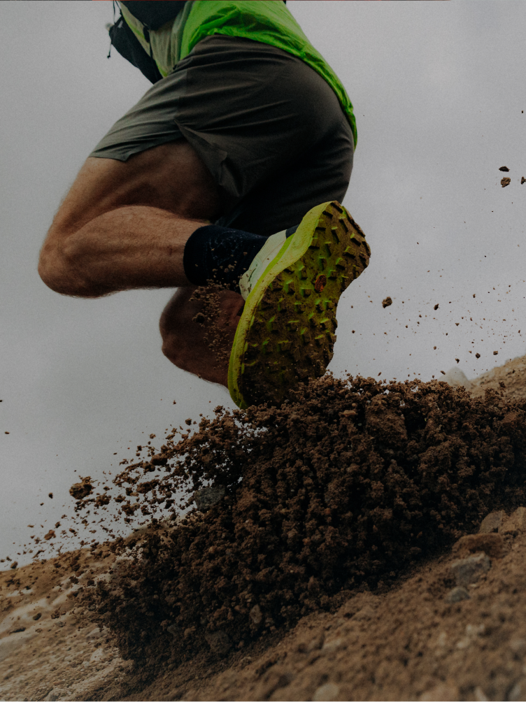 Runner's foot in a bright green trail shoe kicking up dirt.