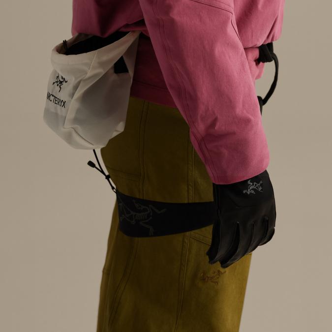 A person wears a pink jacket, olive pants, a white Arc'teryx pouch, and a black Arc'teryx glove.