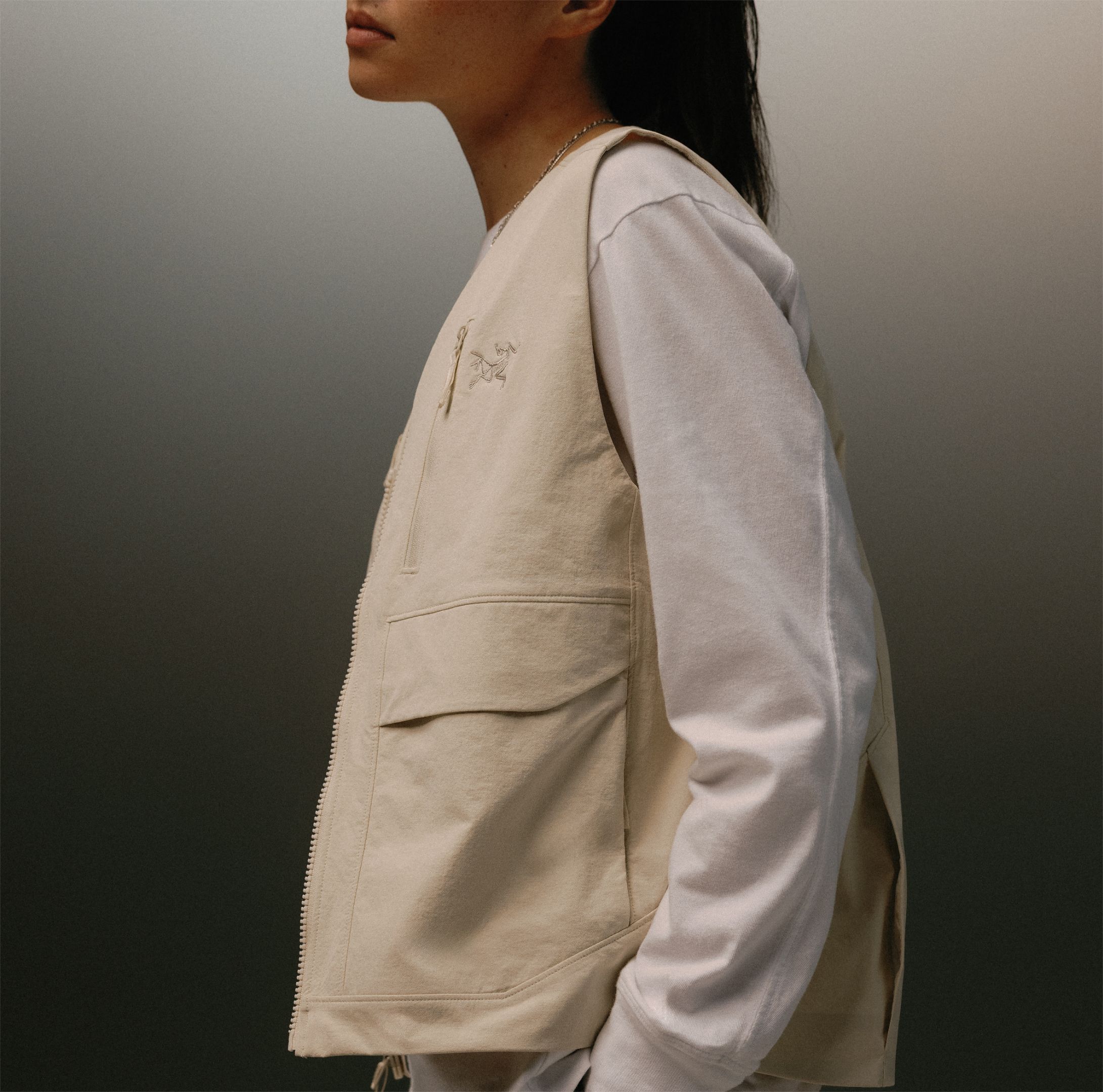 Side profile of a person wearing a beige Arc'teryx utility vest over a white long-sleeve shirt.