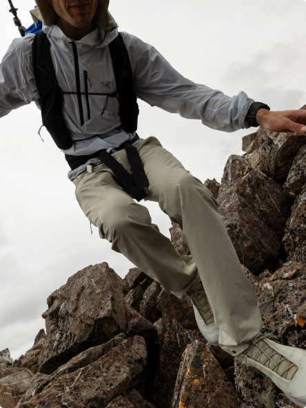 A person in light grey outdoor gear scrambles over jagged dark rocks.