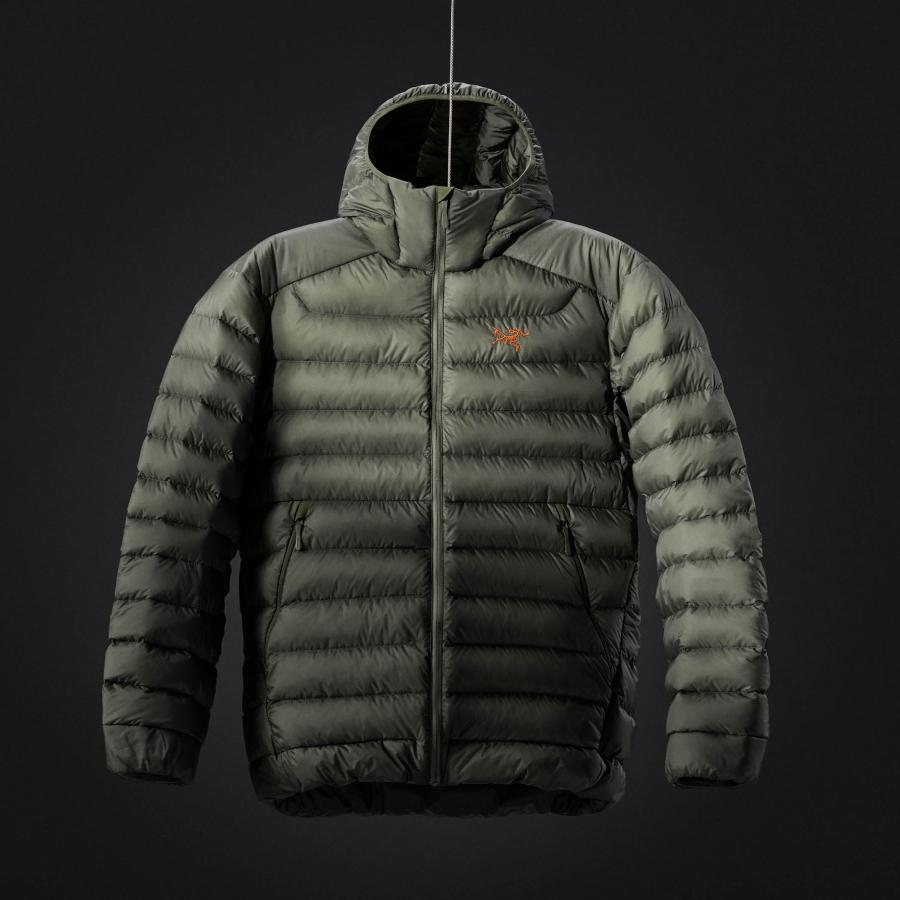 a green padded jacket with a hood is hanging from a string on a black background .
