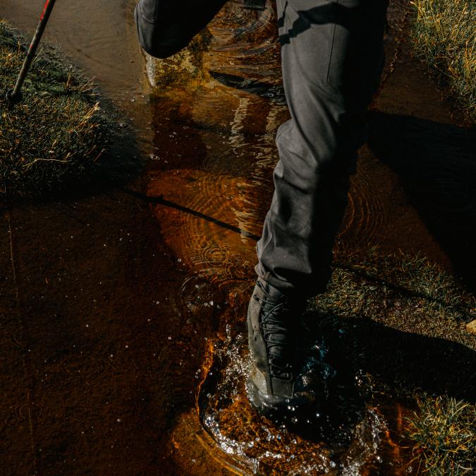 A person's hiking boot splashing in a shallow stream with a hiking pole visible.