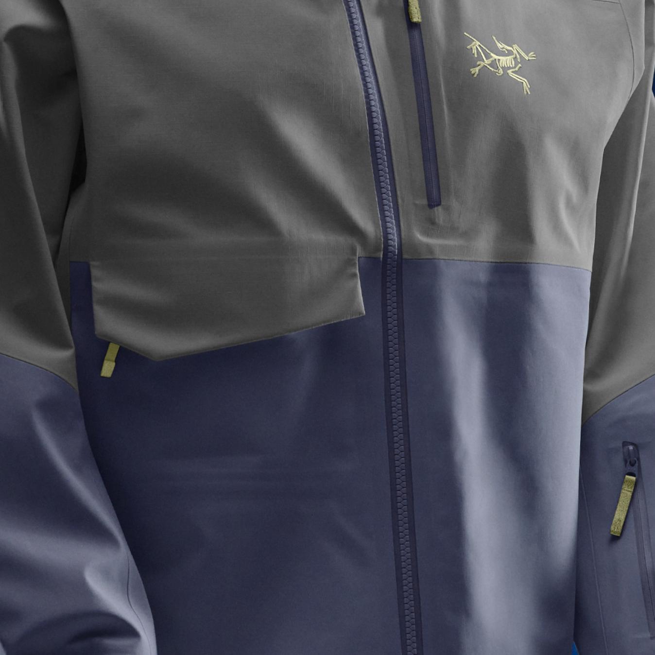 A two-toned grey and blue jacket with an Arc'teryx logo, zippers, and pockets.