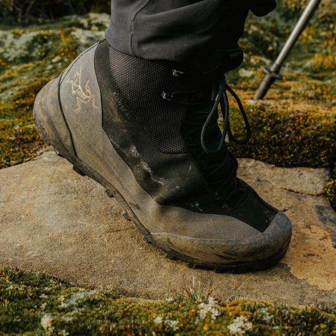 A muddy Arc'teryx Konseal hiking boot on a rock.