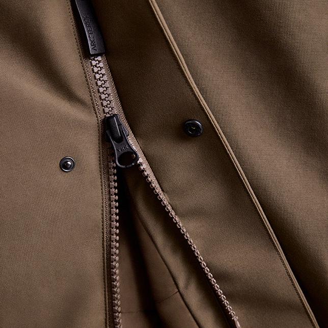 Partially unzipped brown jacket showing a YKK zipper pull, an Arc'teryx branded tab, and two snap buttons.
