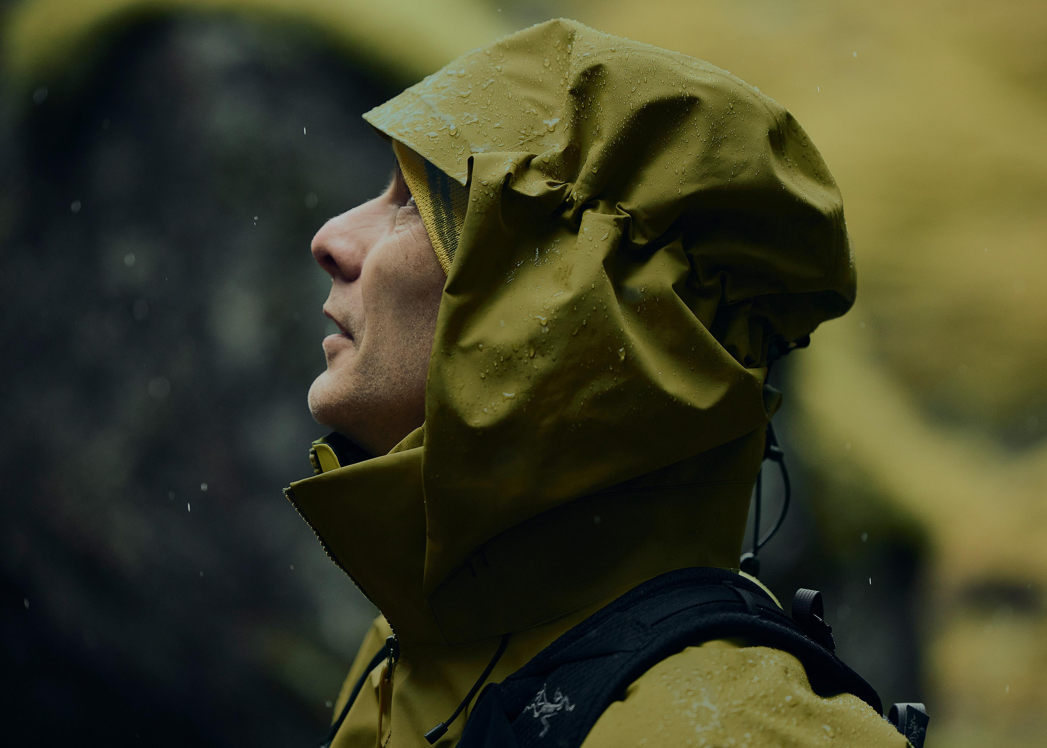 a man wearing a yellow raincoat with a hood is standing in the rain .