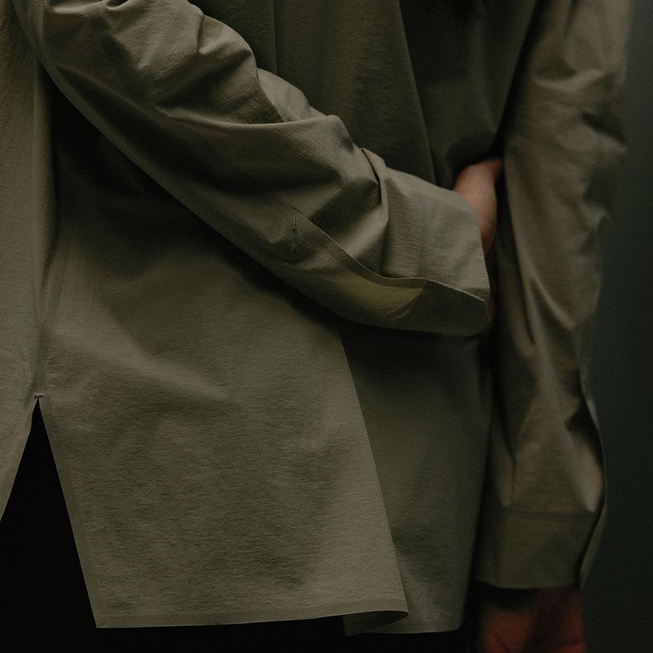 A person from behind wearing a muted green long-sleeved shirt, with one hand tucked behind their back.