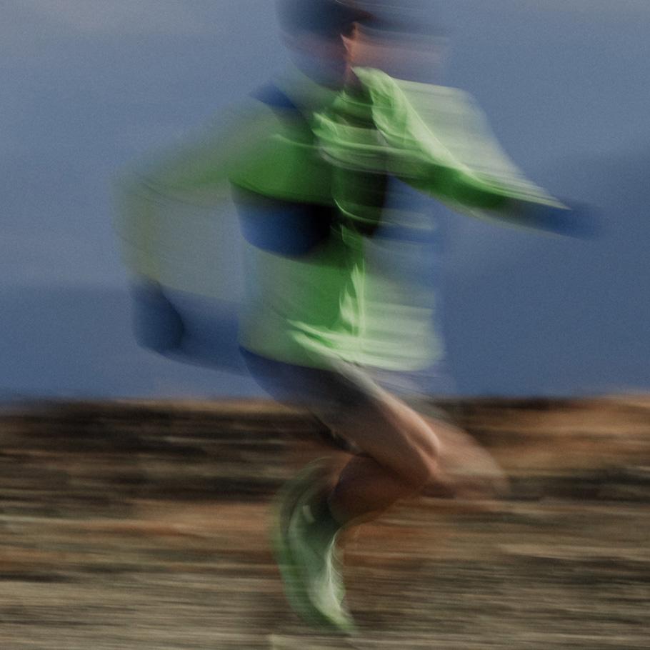 Motion-blurred image of a person in a green shirt running outdoors.