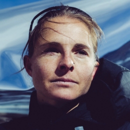 Close-up of a woman with a nose piercing looking up, against a blue sky.