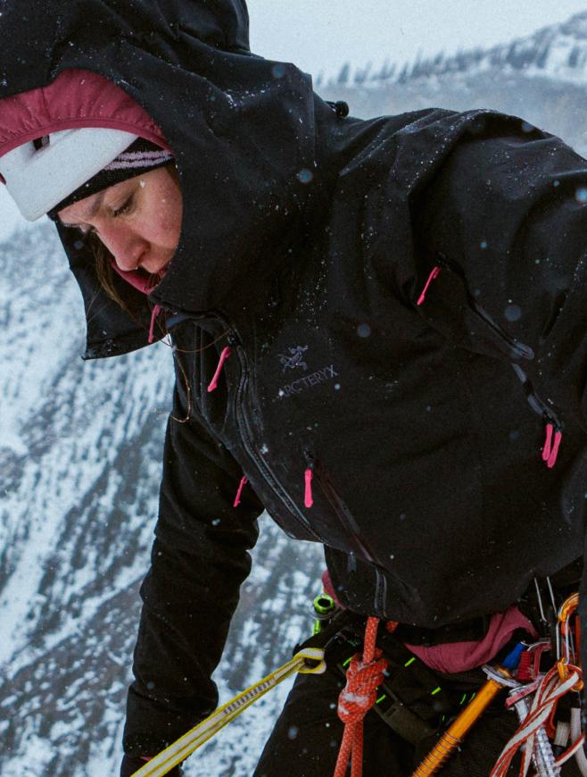 A climber in a black jacket and helmet descends a snowy mountain during a snowfall.