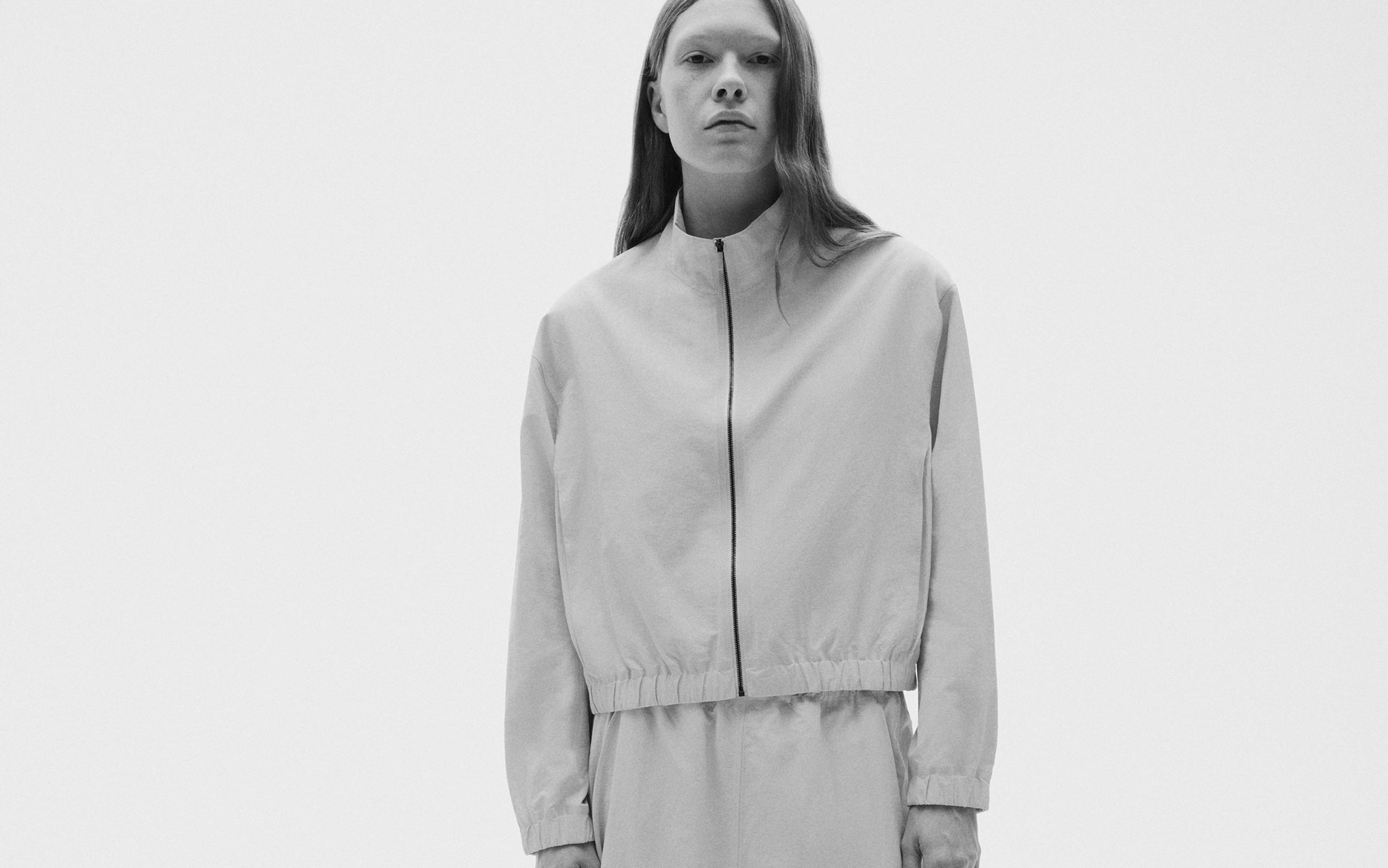 Black and white photo of a woman in a light-colored zip-up jacket and matching pants.