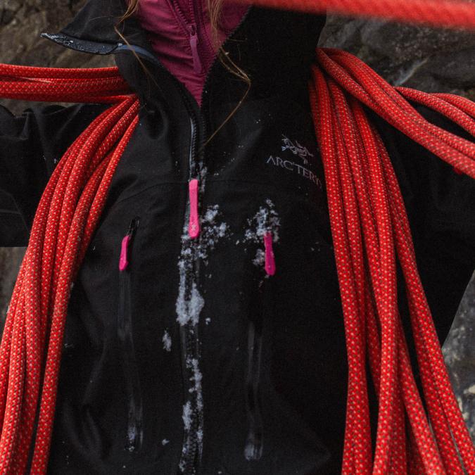 Person in black Arc'teryx jacket with snow and red climbing rope.