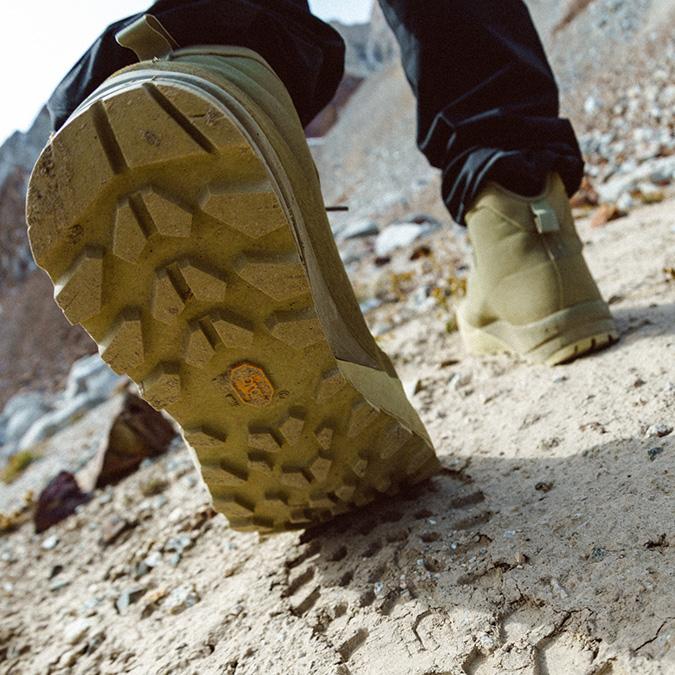Heavily-treaded sole of a hiking boot stepping on a dusty trail.