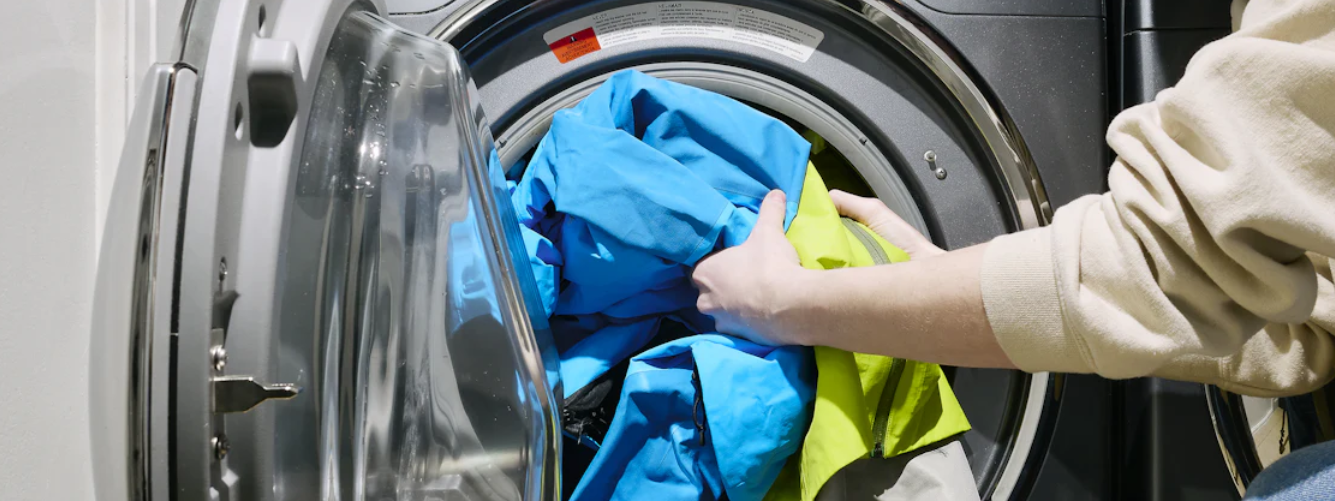 Hands loading colorful clothes into a front-loading washing machine.
