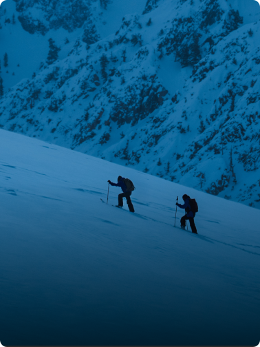 Aerial view of a skier carving a turn in deep blue snow, kicking up a large plume of powder.