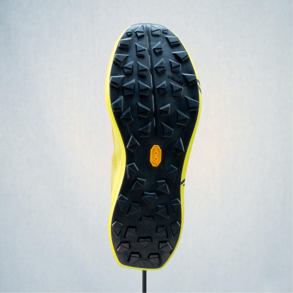 Sole of a yellow trail running shoe with black Vibram lugs.