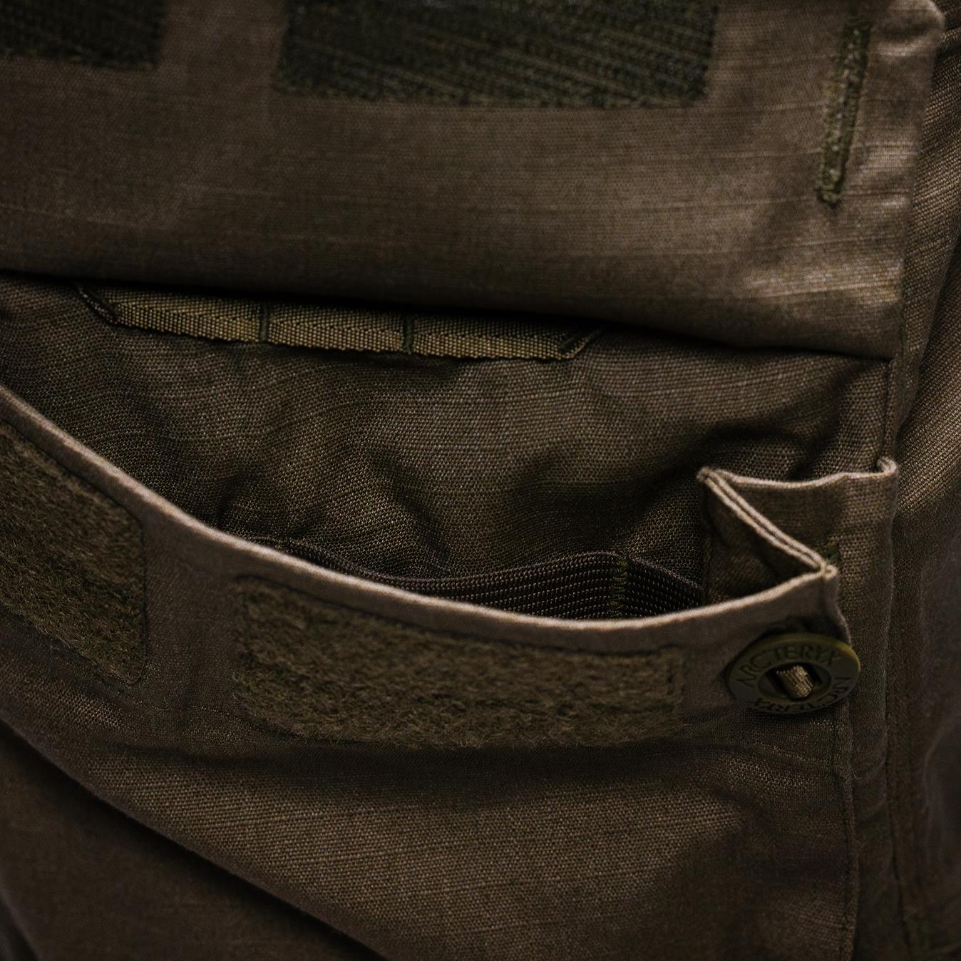 Close-up of dark green ripstop fabric on a cargo pocket with an elastic interior, velcro, and an Arc'teryx button.