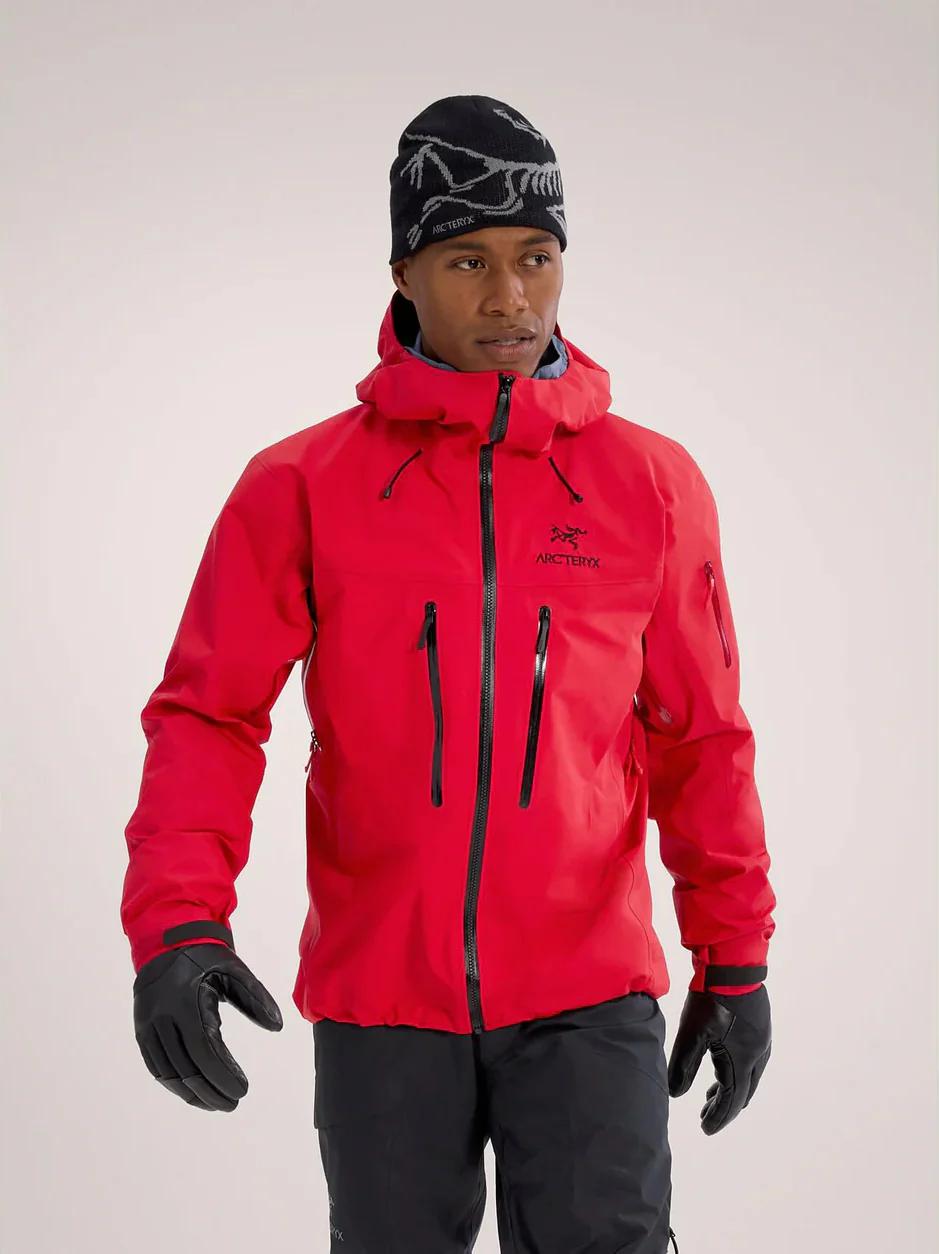 A man wears a red Arc'teryx jacket, black beanie, gloves, and pants.