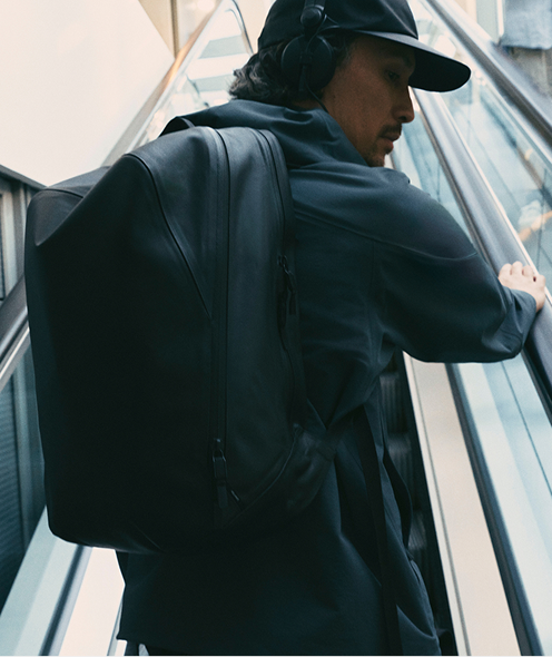 Man with black backpack and headphones on an escalator.