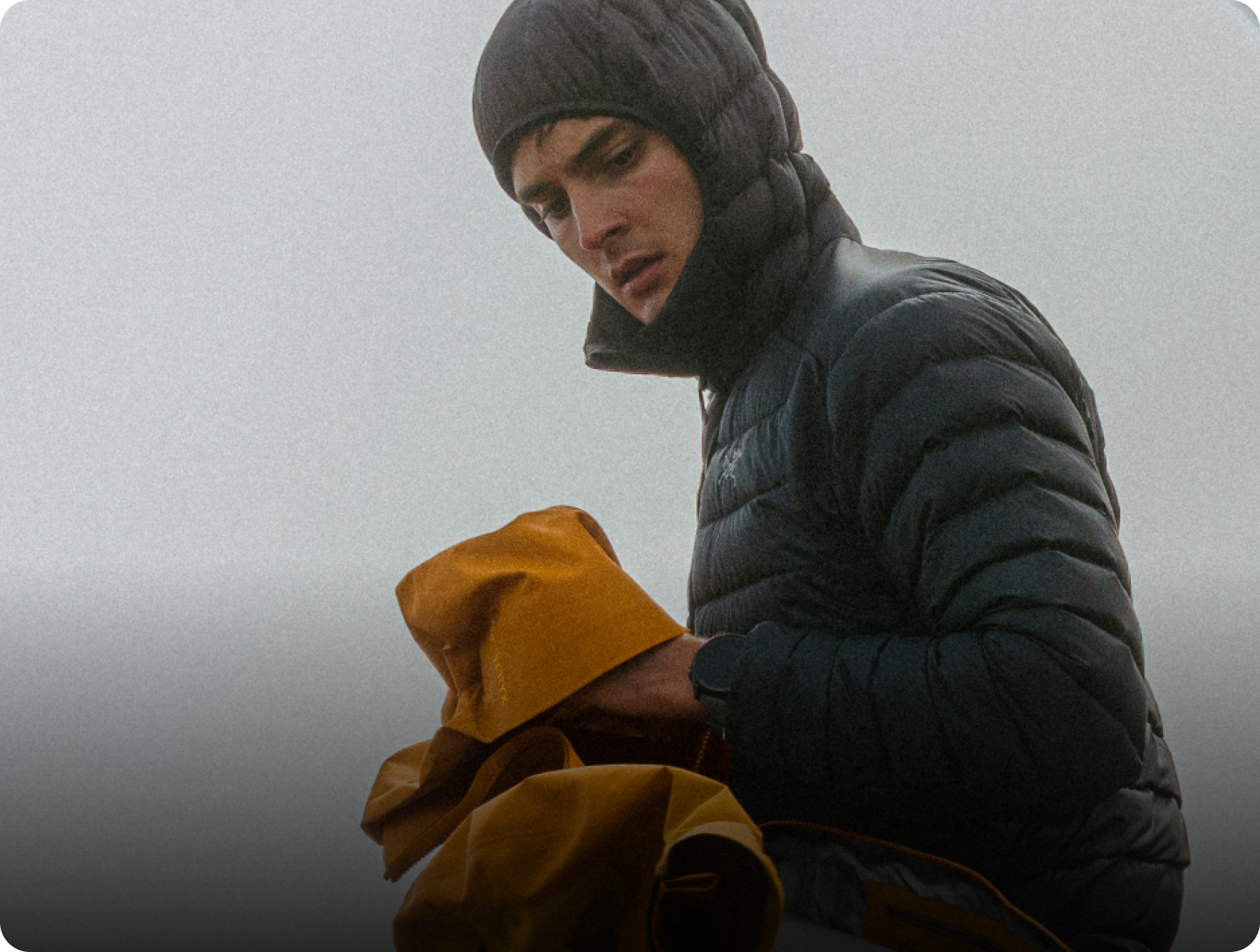 Man in a dark hooded puffer jacket and beanie holds yellow fabric.