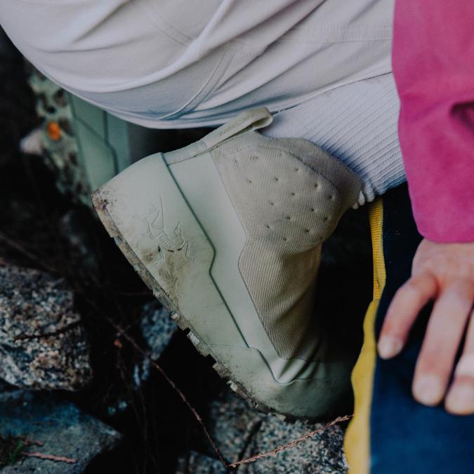 Close-up of a dirty, light green Arc'teryx outdoor shoe on rocky ground.