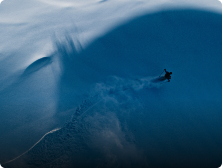 A lone skier descends a steep, shadowy blue snow slope, spraying powder.