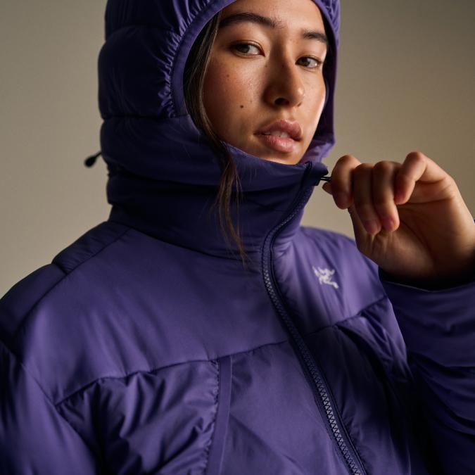 A woman in a purple Arc'teryx hooded jacket adjusts a drawstring at her neck.